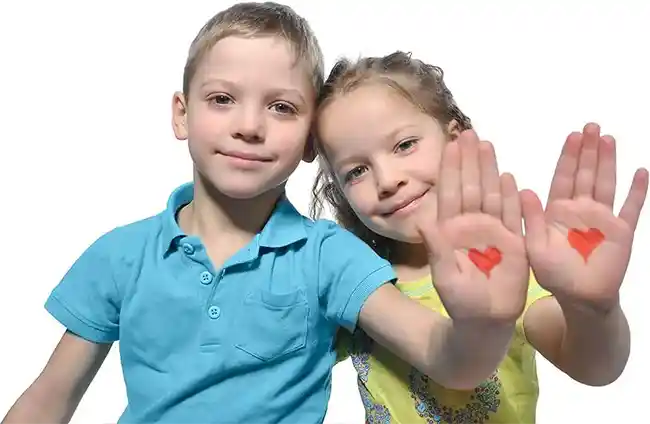 Two children smiling and showing their palms with red heart drawings on them.